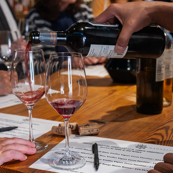 Person pouring red wine into a glass at a wine tasting event.